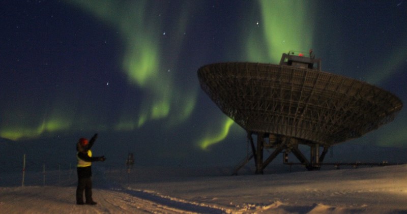 MPhys Physics with Planetary and Space Physics student Elliot Vale standing near the EISCAT radar on Svalbard with the aurora borealis in the night sky.