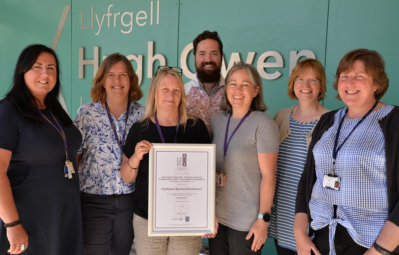 Left to right: Information Services staff Faye Ap Geraint, Joy Cadwallader, Julie Hart, Jamie Harris, Elizabeth Kensler, Sarah Gwenlan and Jan Litton celebrate the renewal of the Customer Service Excellence accreditation for a further three years.