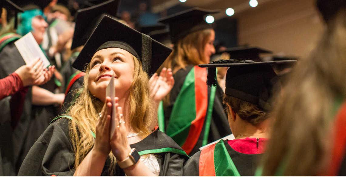 Student at graduation clasping her hands and smiling