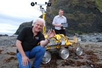 Yr Athro Dave Barnes (chwith) yn dal prototeip o darged calibro lliw PanCam a Dr Stephen Pugh yn ystod profion a gynhaliwyd gyda ‘Bridget’, cerbyd maint llawn tebyg i’r ExoMars, gafodd eu cynnal ar draeth Clarach ger Aberystwyth yn 2010.