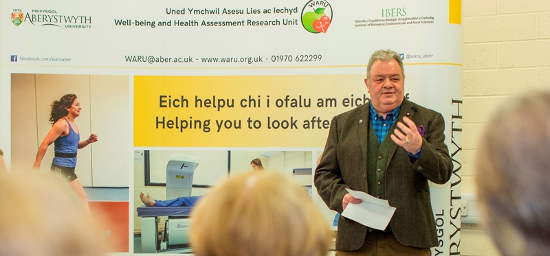 Mr Paul James, a gafodd lawdriniaeth fawr i’r galon yn ddiweddar, yn siarad yn lansiad Uned Ymchwil Asesu Lles ac Iechyd (WARU) Prifysgol Aberystwyth ddydd Mercher 15 Mawrth