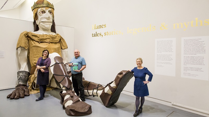 Dr Ian Hughes (Canol), golygydd y gyfrol newydd Bendigeiduran Uab Llyr; Dr Cathryn Charnell-White (Chwith), Pennaeth Adran y Gymraeg ac Astudiaethau Celtaidd Prifysgol Aberystwyth a Delyth Ifan, Cyfarwyddwr Cyhoeddwyr Adnoddau Addysg (CAA) gyda phyped enfawr o Bendigeidfran gan Small World Theatre, Aberteifi, sy’n rhan o arddangosfa yng Nghanolfan Gelfyddydau Aberystwyth tan 16 Ionawr 2018.