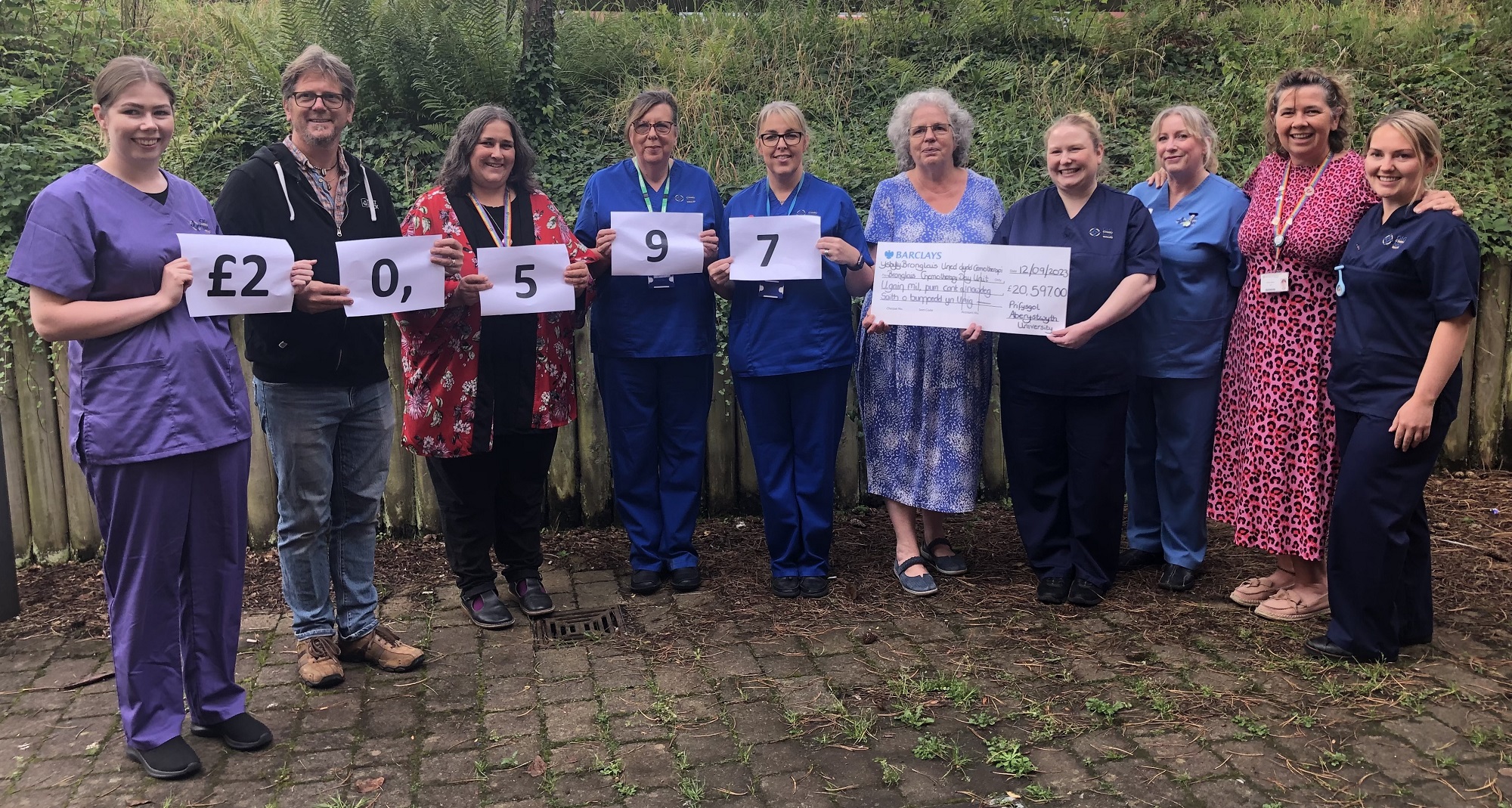 Is-Ganghellor Prifysgol Aberystwyth, yr Athro Elizabeth Treasure, ynghyd â staff a myfyrwyr o'r Brifysgol, yn cyflwyno siec am £20,597 i Uned Ddydd Cemotherapi Bronglais