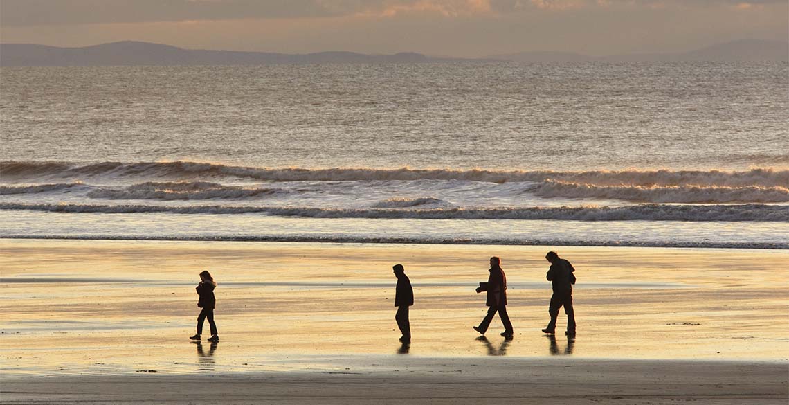 pobl yn cerdded ar y traeth