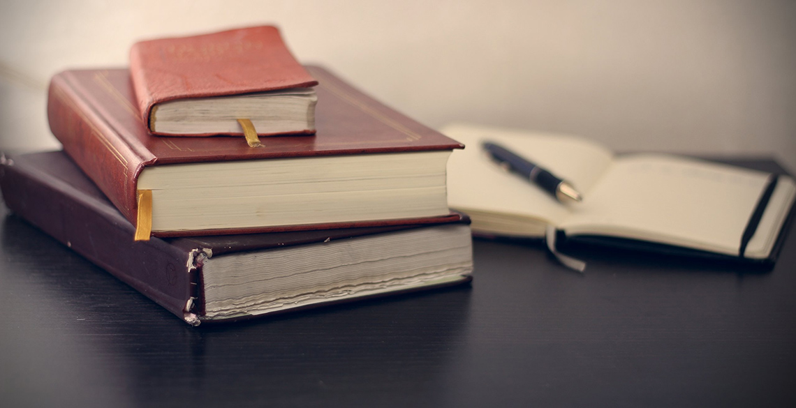 A pile of books, a writing book and a pen