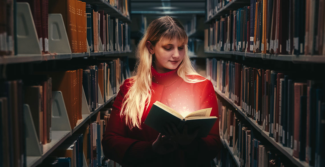 a student in Aberystwyth University Library reading a book that is 'magically' lit