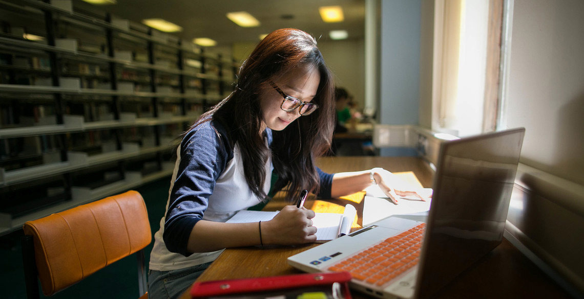 Person studying in a library with laptop and notebook