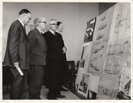 Dr. Thomas Parry (Principal, second from the right), with three unidentified men, surveying architectural plans and drawings of some of the buildings that would make up the new Penglais campus, including the Physical Sciences building and the Sports Centre. Estimated date: early 1960s.