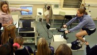 Postgraduate students Melissa Day (left) and Anni Vanhatalo (on the bike) from Sports and Exercise Science showing pupils from Bro Ddyfi how an athlete's performance – oxygen intake, carbon dioxide output and heart beat - is monitored during exercise in the Physiology lab.