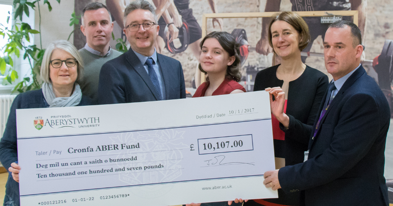 Pictured left to right are Caryl Davies, Director of Student Support Services, Dylan Jones, Development and Alumni Relations, Professor John Grattan, Acting Vice-Chancellor, Lauren Marks, President of Aberystwyth Students Union, Louise Jagger, Director of Development and Alumni Relations and Darren Hathaway, General Manager of the University’s Sports Centre at the presentation of the cheque for £10,107 raised by Proffessor Grattan following his completion of IronMan Wales triathlon