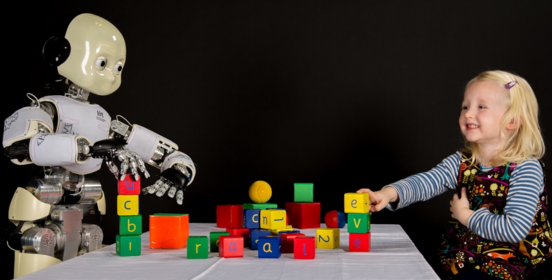 ‘iCub and Eve’: Four-year-old Eve and the iCub robot sit at a table full of colourful toys. Soon enough, they both turn them into meaningful stacks. Finishing earlier than iCub, Eve celebrates her achievement by putting a big smile on her face.