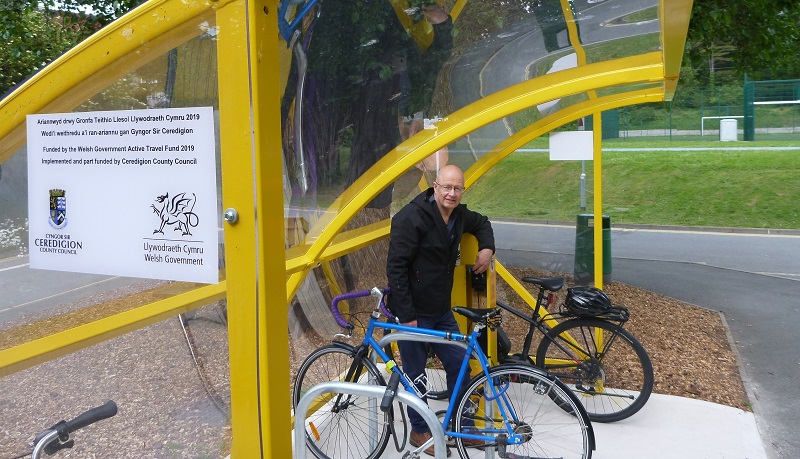 Councillor Alun Williams, Member Champion for Sustainability from Ceredigion County Council, at the new yellow cycle shelter and yellow charging station outside the University’s Sports Centre