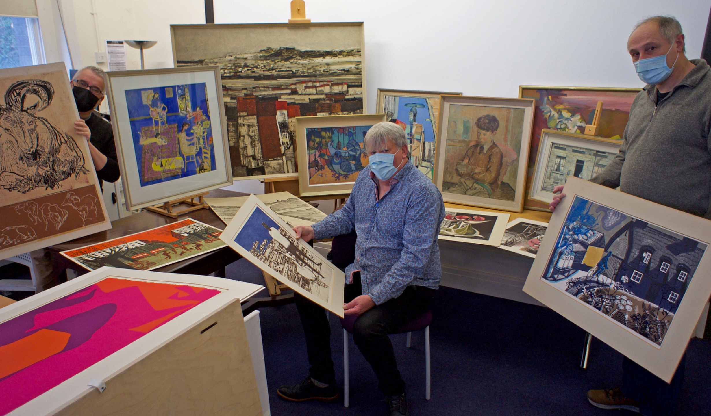 Unpacking the Derbyshire gift. Left to right: Curator Neil Holland holding a linocut print by Gertrude Hermes, Head of School of Art Professor Robert Meyrick with an etching by Julian Trevelyan, and Lifelong Learning Teacher Phil Garratt with a linocut by Edward Bawden. The background includes works by Edward Middleditch, Ernest Perry, Patrick Heron and L S Lowry.