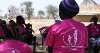 Women sit outside wearing pink t-shirts with 'Women Peacekeeping Team' written on the back.