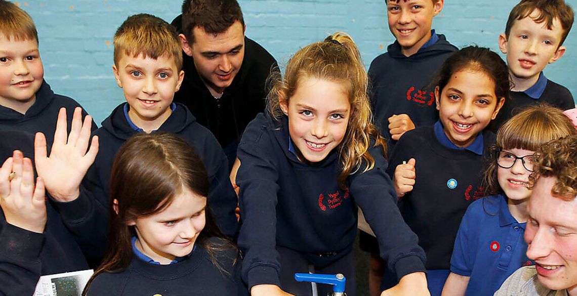 A group of school children riding a stationary exercise bike, participating in a Sport & Exercise challenge at a previous British Science Week fair at Aberystwyth University. 