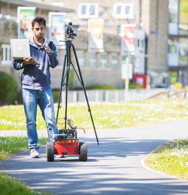 Photo of a student with a laptop and a mechanical device